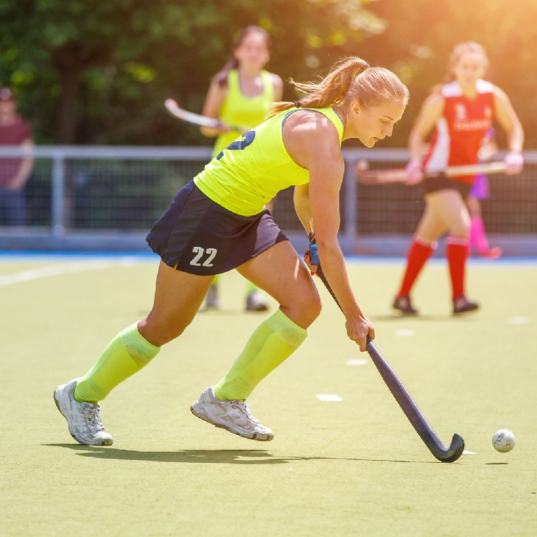 Hockey player dribbling with hockey stick on a pitch with other players in the background