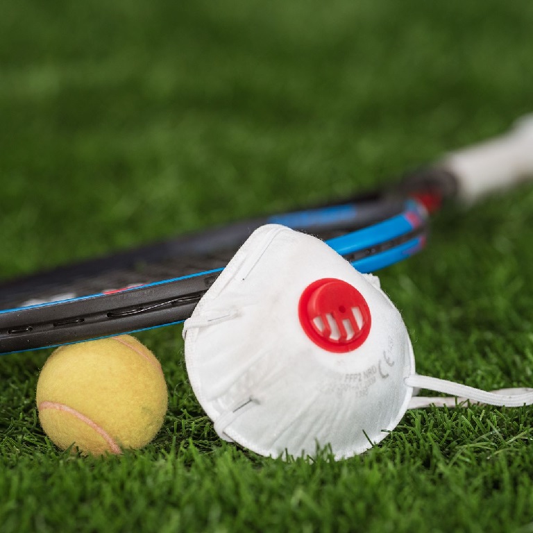 Close-up of tennis ball and racquet on grass with a facemask