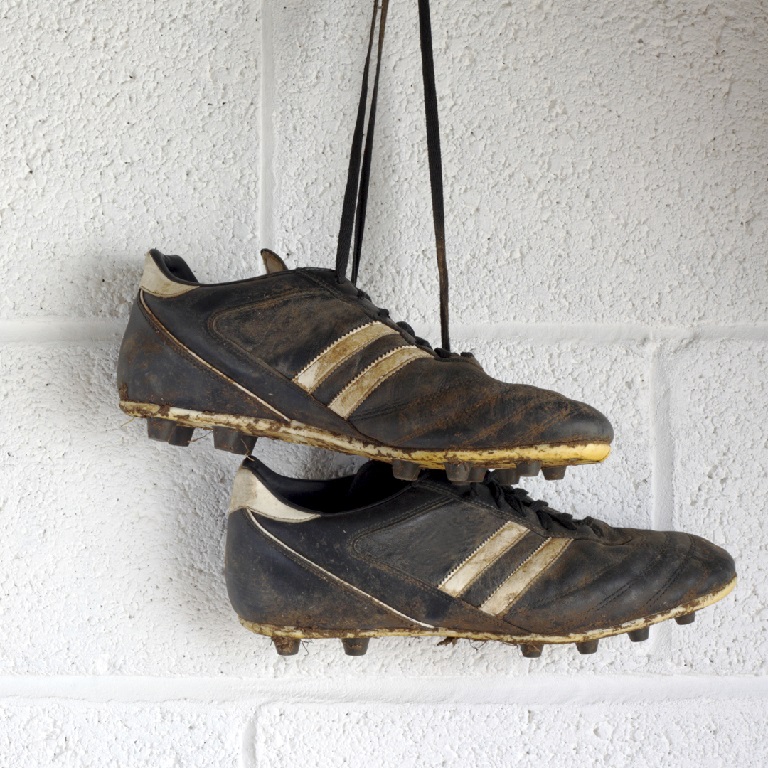 Pair of muddy black football boots hanging on a white brick wall