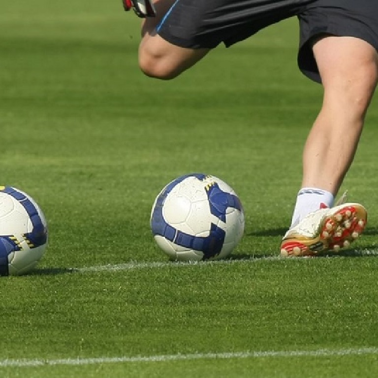 Football players legs, about to kick one ball in a line