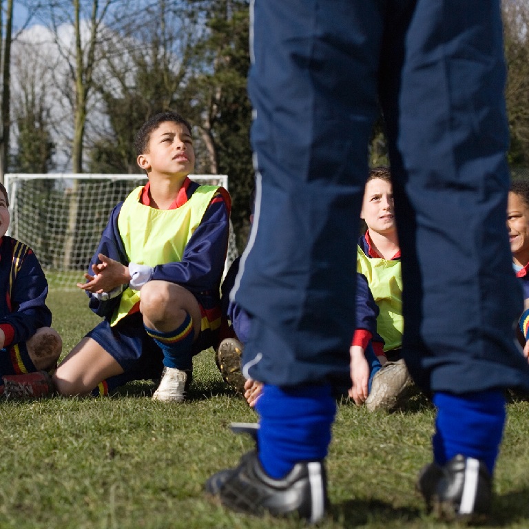 Kids kneeling or sitting on the ground listening to football coach