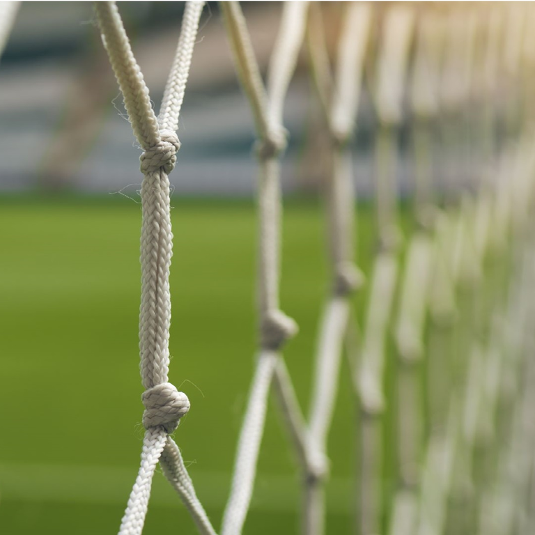 Close-up of a football net with a blurred green pitch in the background, symbolising safeguarding for sports activities.